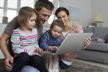 Happy family of four using laptop in living room - RBYF000498