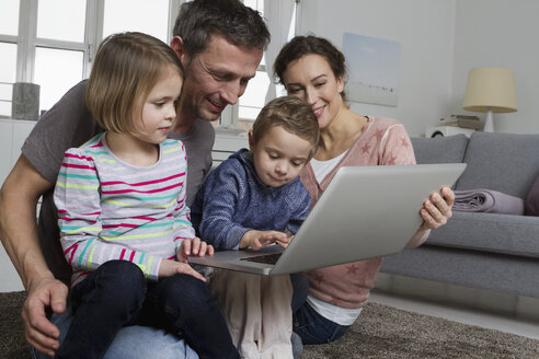 Glückliche vierköpfige Familie mit Laptop im Wohnzimmer - RBYF000498