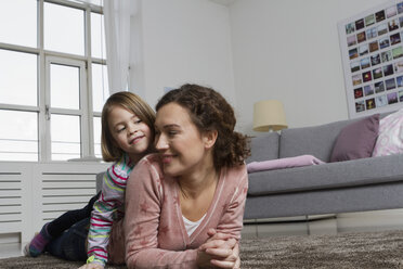 Happy mother and daughter lying on carpet in living room - RBYF000427