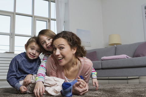Glückliche Mutter, Sohn und Tochter liegen auf dem Teppich im Wohnzimmer, lizenzfreies Stockfoto