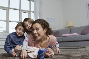 Happy mother, son and daughter lying on carpet in living room - RBYF000429