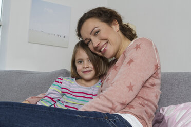 Happy mother and daughter sitting on couch - RBYF000430