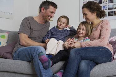 Happy family of four sitting on couch - RBYF000433