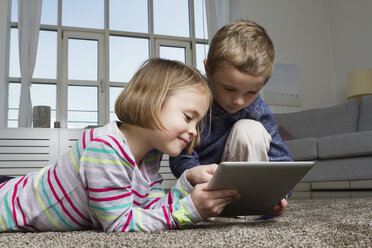 Bruder und Schwester benutzen Tablet-Computer auf dem Teppich im Wohnzimmer - RBYF000434