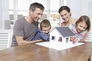 Family of four looking at house model - RBYF000450