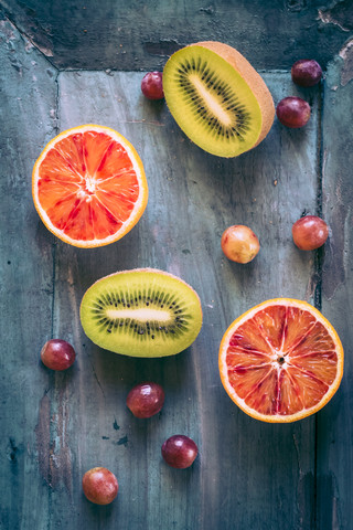 Blaue Trauben und zwei Hälften von Blutorange und Kiwi auf blauem Holzgrund, lizenzfreies Stockfoto