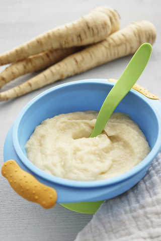 Bowl of parsnip puree, parsnips and cloth on wooden table stock photo