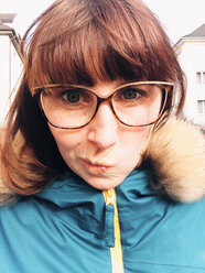 Frau mit Brille und blauer Jacke macht ein lustiges Gesicht in die Kamera, Bonn, NRW, Deutschland - MEAF000136