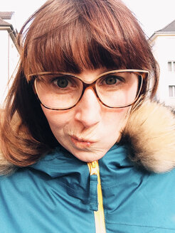 Women with glasses and blue jacket making a funny face at camera, Bonn, NRW, Germany - MEAF000136