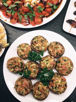 Stuffed mushrooms on a buffet plate next to tomatoes - MEAF000157