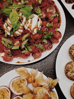 Tomate-Mozzarella auf einem Teller neben Passionsfrüchten und Physalis auf einem Buffet - MEAF000158