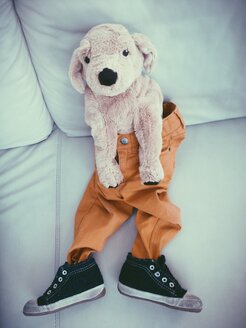 Plush dog wearing child pants and shoes on couch - MEAF000163