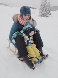 Mutter und Sohn fahren auf einem Schlitten den verschneiten Berg hinunter in Reit im Winkl, Bayern, Deutschland - MEAF000186