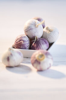 Knoblauch in einer Schüssel und auf einem Holztisch - MAEF007913