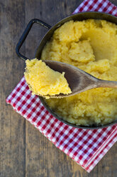 Iron cooking pot and wooden spoon of cooked Polenta on kitchen towel and wooden table - LVF000713