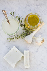 Zwei Stücke Schafskäse, ein Glas Olivenöl, Knoblauchzwiebeln, Rosmarin und ein Glas Salzlake auf weißem Marmor - LVF000728