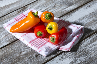 Red, orange and yellow bell peppers on kitchen towel and wooden table - MAEF007958