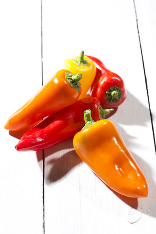 Rote, orangefarbene und gelbe Paprikaschoten auf weißem Holztisch, lizenzfreies Stockfoto