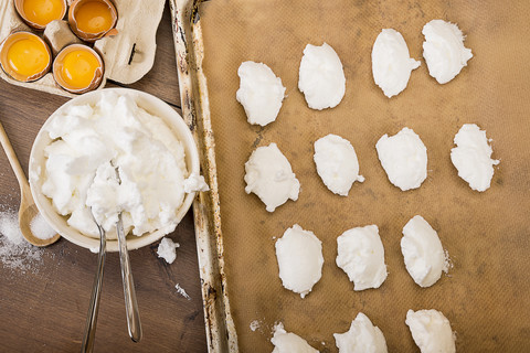 Schüssel mit Eischnee für Baisers und geformte rohe Baisers auf dem Backblech, lizenzfreies Stockfoto