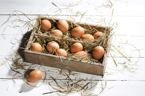 Holzkiste mit braunen Eiern und Heu auf weißem Holztisch, lizenzfreies Stockfoto
