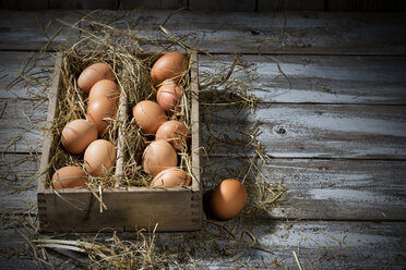 Holzkiste mit braunen Eiern und Heu auf grauem Holztisch - MAEF007942