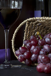 Weidenkorb mit roten Weintrauben (vitis vinifera), Rotweinglas und Flasche im Hintergrund - YFF000046