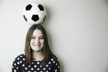 Porträt eines lächelnden Teenagers mit Fußball auf dem Kopf vor einer weißen Wand - JATF000671