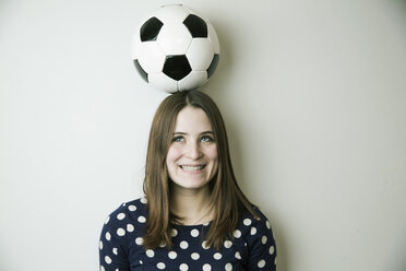 Porträt eines lächelnden Teenagers mit Fußball auf dem Kopf vor einer weißen Wand - JATF000670