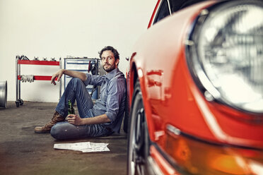 Man with a bottle of beer leaning against his vintage car - SE000570