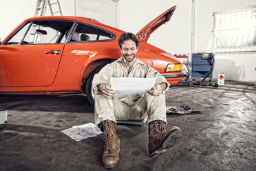 Smiling man with construction plan leaning against his vintage car - SE000568