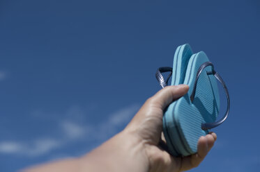 Hand holding pair of light blue flip-flops in front of sky - ASF005271