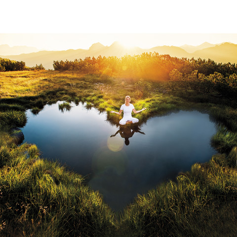 Österreich, Land Salzburg, Altenmarkt-Zauchensee, meditierende Frau am Teich, lizenzfreies Stockfoto