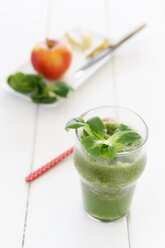 Glass of apple lamb's lettuce smoothie, bowl, apple, kitchen knife and spoon on white wooden table - EVGF000393