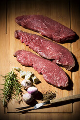 Beefsteak, garlic, rosemary, herb butter and pepper on chopping board - MAEF007988