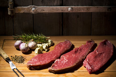 Beefsteak, garlic, rosemary, herb butter and pepper on chopping board - MAEF007987