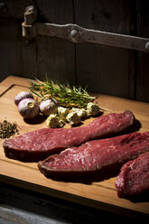 Beefsteak, garlic, rosemary, herb butter and pepper on chopping board - MAEF007986