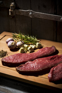 Beefsteak, Knoblauch, Rosmarin, Kräuterbutter und Pfeffer auf dem Schneidebrett - MAEF007986