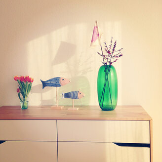 Transparent green flower vase with two twigs of hollies (Ilex aquifolium), water glass of tulips and decoration on sideboard - AFF000027