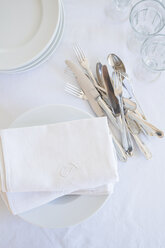 Glasses, plates, silver cutlery and cloth napkins on white table cloth, elevated view - LVF000779