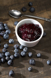 Bowl of blueberry and raspberry jam, spoon and blueberries on dark wooden table - MAEF008018