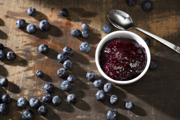 Bowl of blueberry and raspberry jam, spoon and blueberries on dark wooden table - MAEF008017