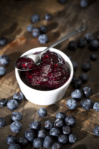 Schale mit Heidelbeer- und Himbeermarmelade, Löffel und Heidelbeeren auf dunklem Holztisch, lizenzfreies Stockfoto