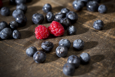 Heidelbeeren und zwei Himbeeren auf dunklem Holztisch - MAEF008013