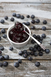 Bowl of blueberry and raspberry jam, spoon and blueberries on wooden table - MAEF008011