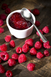 Bowl of raspberry jam, spoon and raspberries on wooden table - MAEF008006