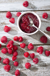 Bowl of raspberry jam, spoon and raspberries on wooden table, elevated view - MAEF008000