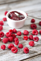 Bowl of raspberry jam, spoon and raspberries on wooden table - MAEF007999