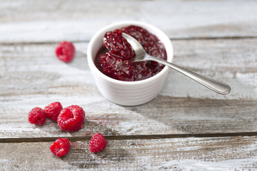 Bowl of raspberry jam, spoon and raspberries on wooden table - MAEF007998