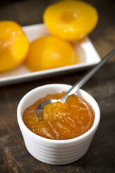 Bowl of peach jam and plate with halves of peaches on wooden table - MAEF008036