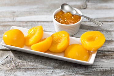 Bowl of peach jam and plate with halves of peaches on wooden table - MAEF008038